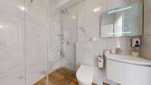 A modern bathroom with a glass shower enclosure, a white toilet, and a vanity with a mirror. - Chrysanta Apartments (Split)