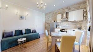 A modern living room with a sofa, a dining table, and chairs. There is a kitchen area with a refrigerator, stove, and cabinets. - Chrysanta Apartments (Split)