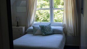 A neatly made bed with a white duvet and two pillows, a bedside table with a lamp, and a window with curtains. - Summer and winter retreat
3 bedrooms - 2 bathrooms (Hatepe)