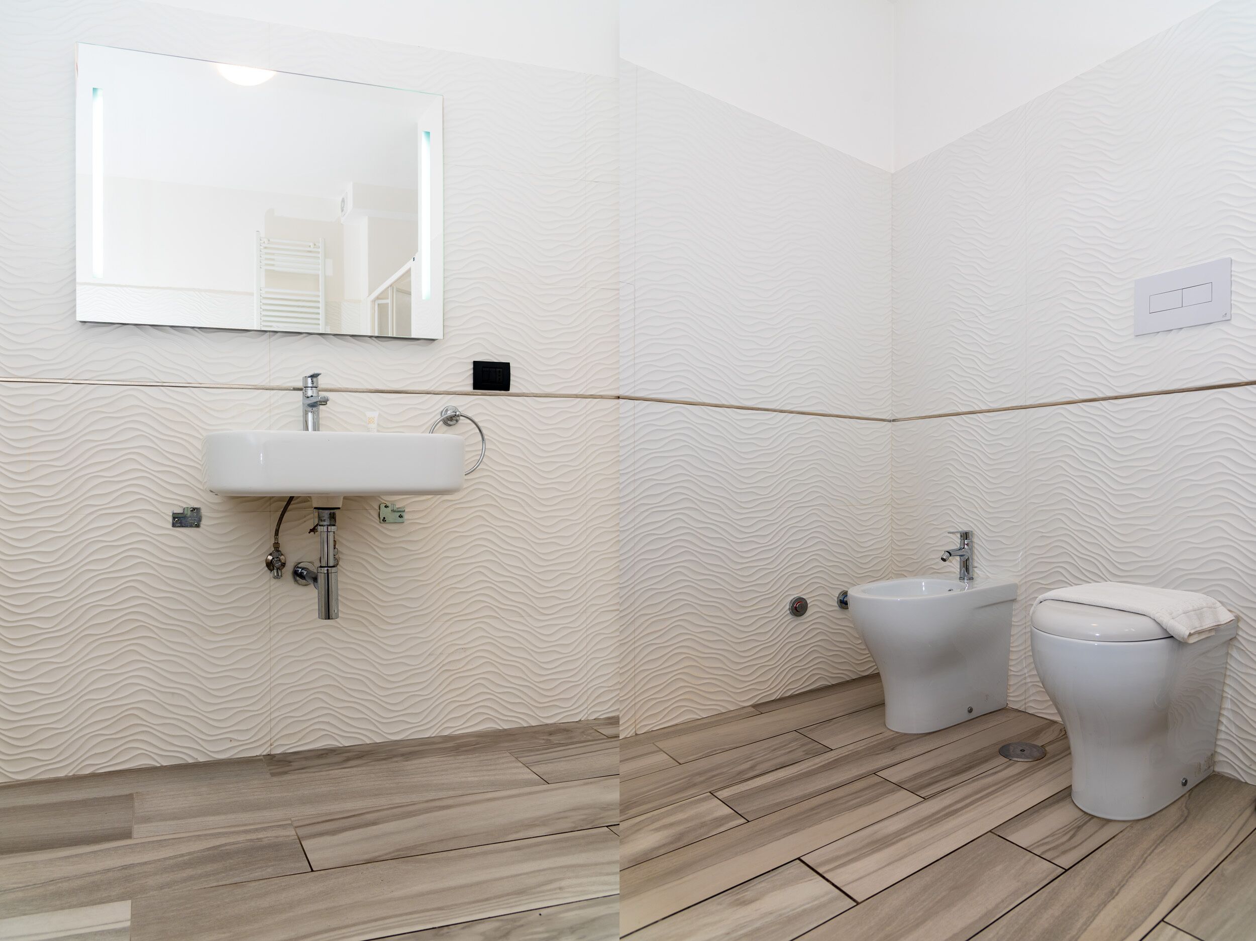 A bathroom with a sink, mirror, bidet, toilet, and patterned walls.