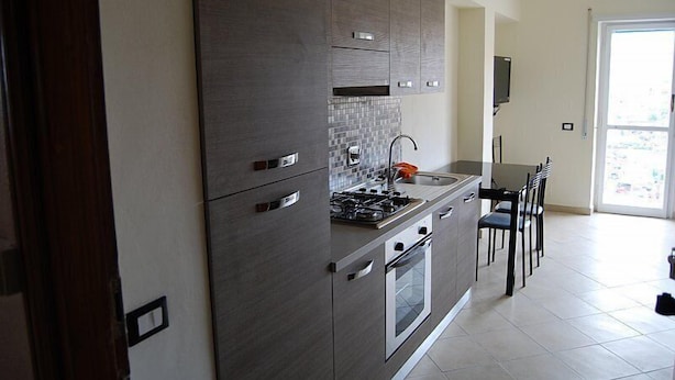 Una cocina moderna con gabinetes grises, una estufa a gas, un horno y un rebozo de azulejos. Hay una zona de comedor con una mesa y sillas.