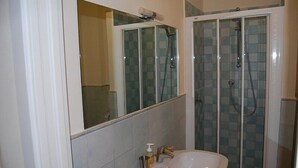 Un baño con cabina de ducha de vidrio, un lavabo con espejo y paredes de azulejos.
