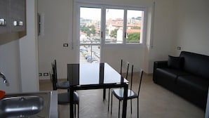 Un espacio habitable compacto con una mesa de comedor, cuatro sillas, un sofá negro y un amplio ventanal con vista a la ciudad.