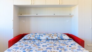 A small room with a bed, a red headboard, and a white wardrobe with two doors and a shelf. - Appartamento Al Centro della Vacanza (Portoferraio)