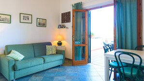 A room with a green sofa, a small table with a lamp, and a dining area with chairs. - Appartamento Il Mare in Cartolina (Portoferraio)