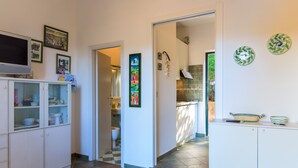 A kitchen with white cabinets, a tiled floor, and a television on the left. - Appartamento Il Mare in Cartolina (Portoferraio)