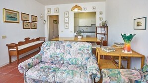 A living room with a sofa, a wooden bench, a dining table with chairs, and a kitchen in the background. - Appartamento Via dei Lecci (Rio)