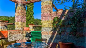 A stone patio with a table and chairs, surrounded by potted plants and a green shutter. - Appartamento Via dei Lecci (Rio)