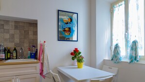 Una cocina con una mesa blanca, sillas, una planta en maceta y un cuadro en la pared.