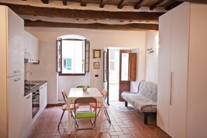 A compact kitchen with a dining table and chairs, a sofa, and a view through an open door. - Le Case di Letizia (Portoferraio)