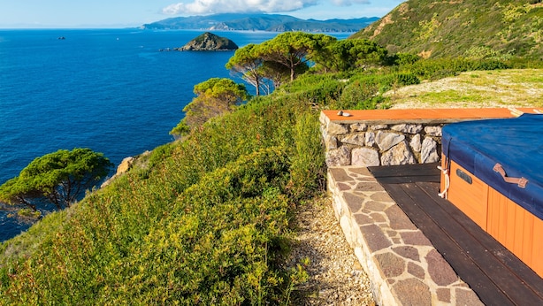 Paisaje costero con un muro de piedra y una terraza de madera con vistas al mar.