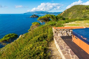 Paisaje costero con un muro de piedra y una terraza de madera con vistas al mar.