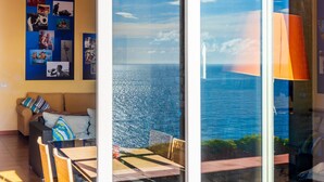 Una habitación con un ventanal grande con vista al mar, un sofá, una mesa de comedor y una pared decorada con varias fotos.