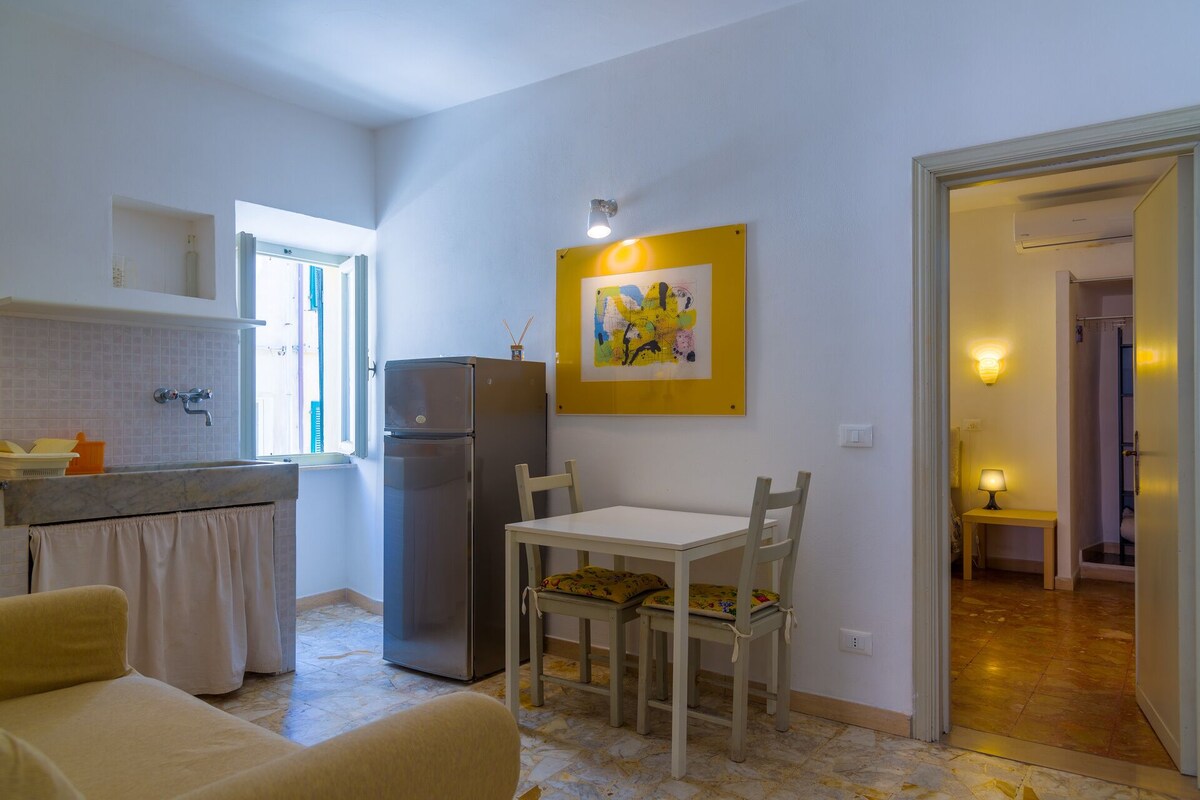 A compact kitchen with a refrigerator, a dining table with chairs, and a painting on the wall.