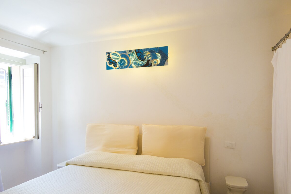 A bedroom with a bed, a window, a toilet, and a wall-mounted artwork.