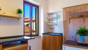 A compact kitchen with wooden cabinets, a countertop, and a window with a view of a building. - Appartamenti Il Grigolo (Portoferraio)