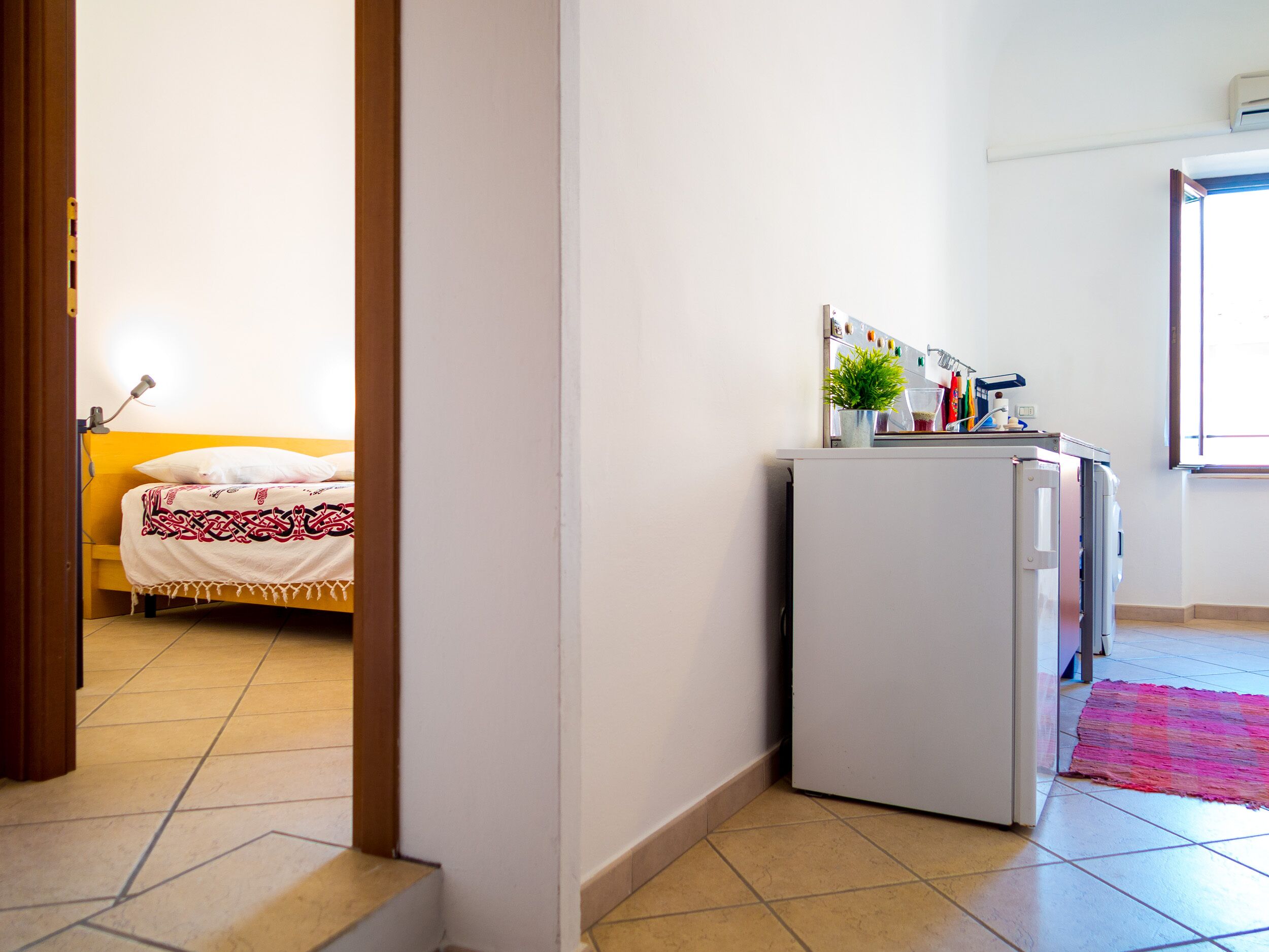 A compact room with a bed, a small kitchenette, and a window.