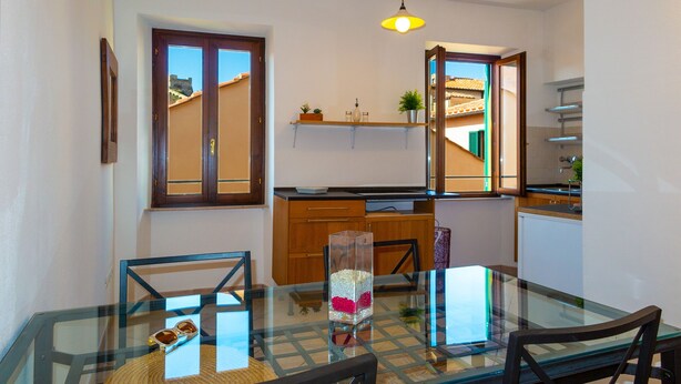 A modern kitchen with wooden cabinets, a glass dining table, and a hanging pendant light. - Appartamenti Il Grigolo (Portoferraio)