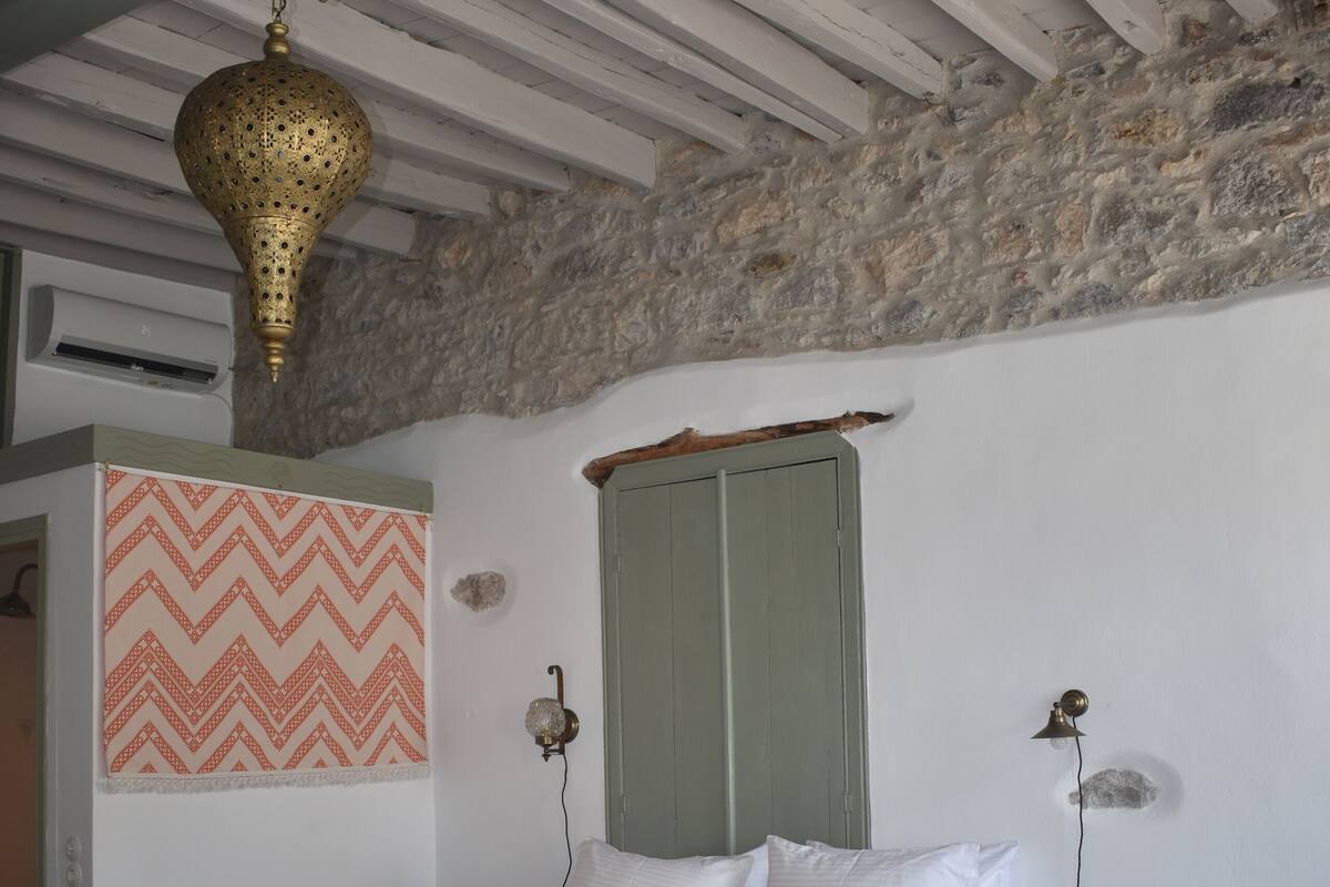 A bedroom with a bed, a wall-mounted lamp, and a patterned wall hanging.