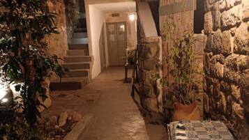 A narrow pathway leading to a door at the end, flanked by stone walls and potted plants.