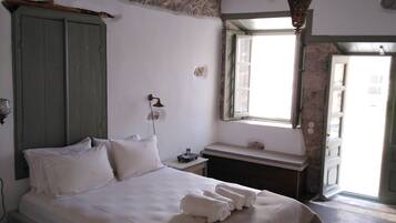 Un dormitorio con cama, mesita de noche, lámpara, ventana y pared de piedra.