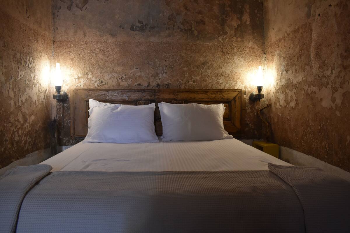 A bed with white linens, two bedside lamps, and a wooden headboard in a room with textured walls.