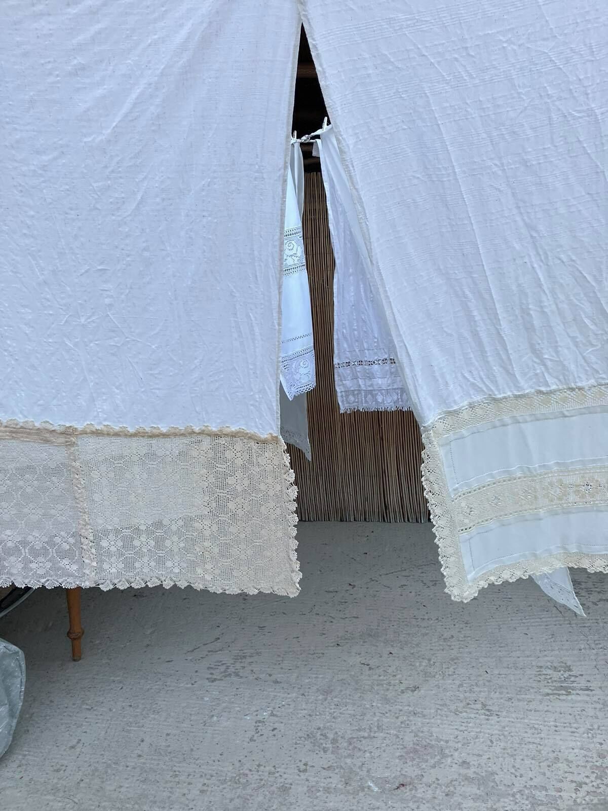 Uma estrutura tipo tenda com borda de renda, piso de madeira e parede listrada verticalmente ao fundo.