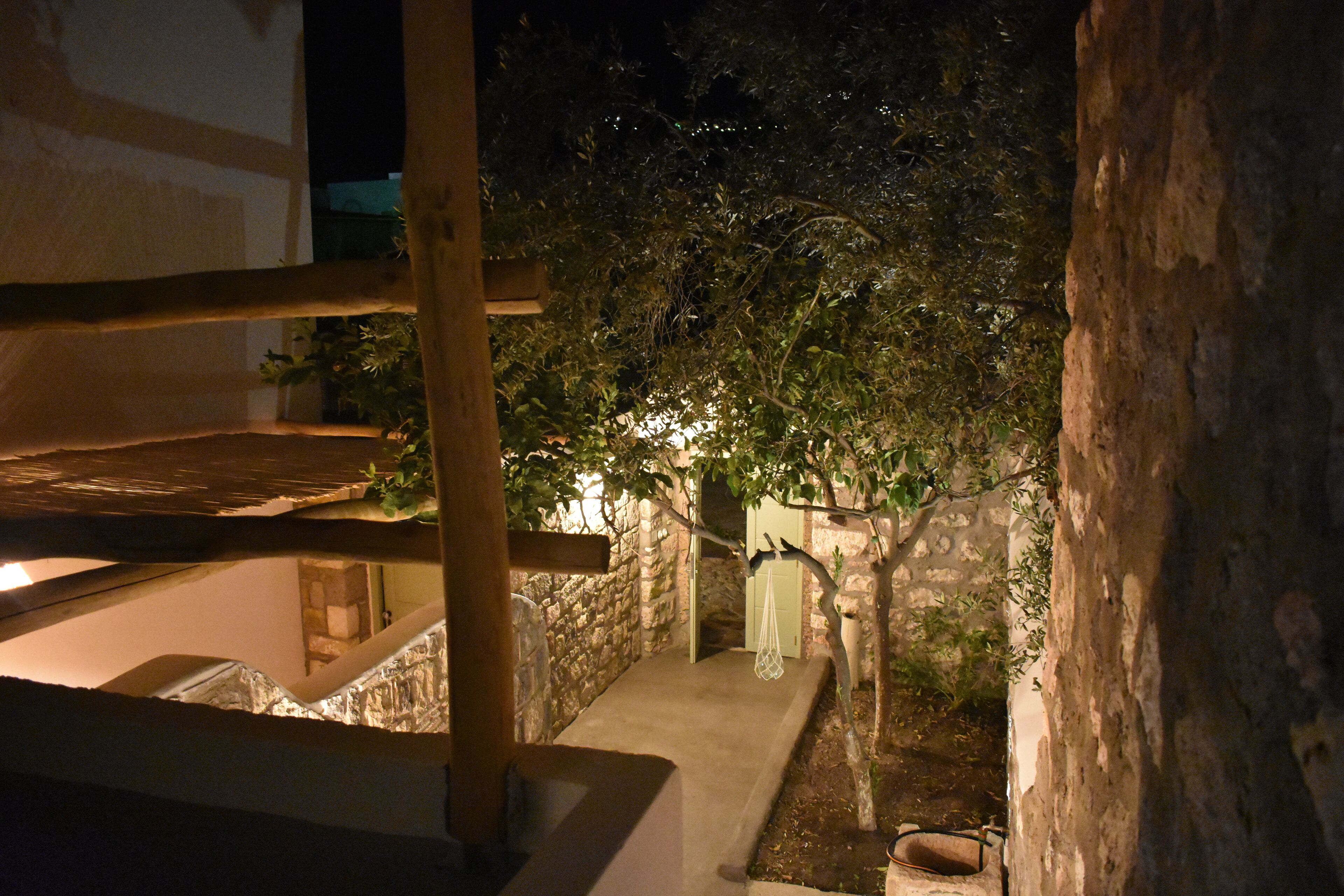 A narrow outdoor corridor with stone walls, a wooden bench, and a hanging plant.