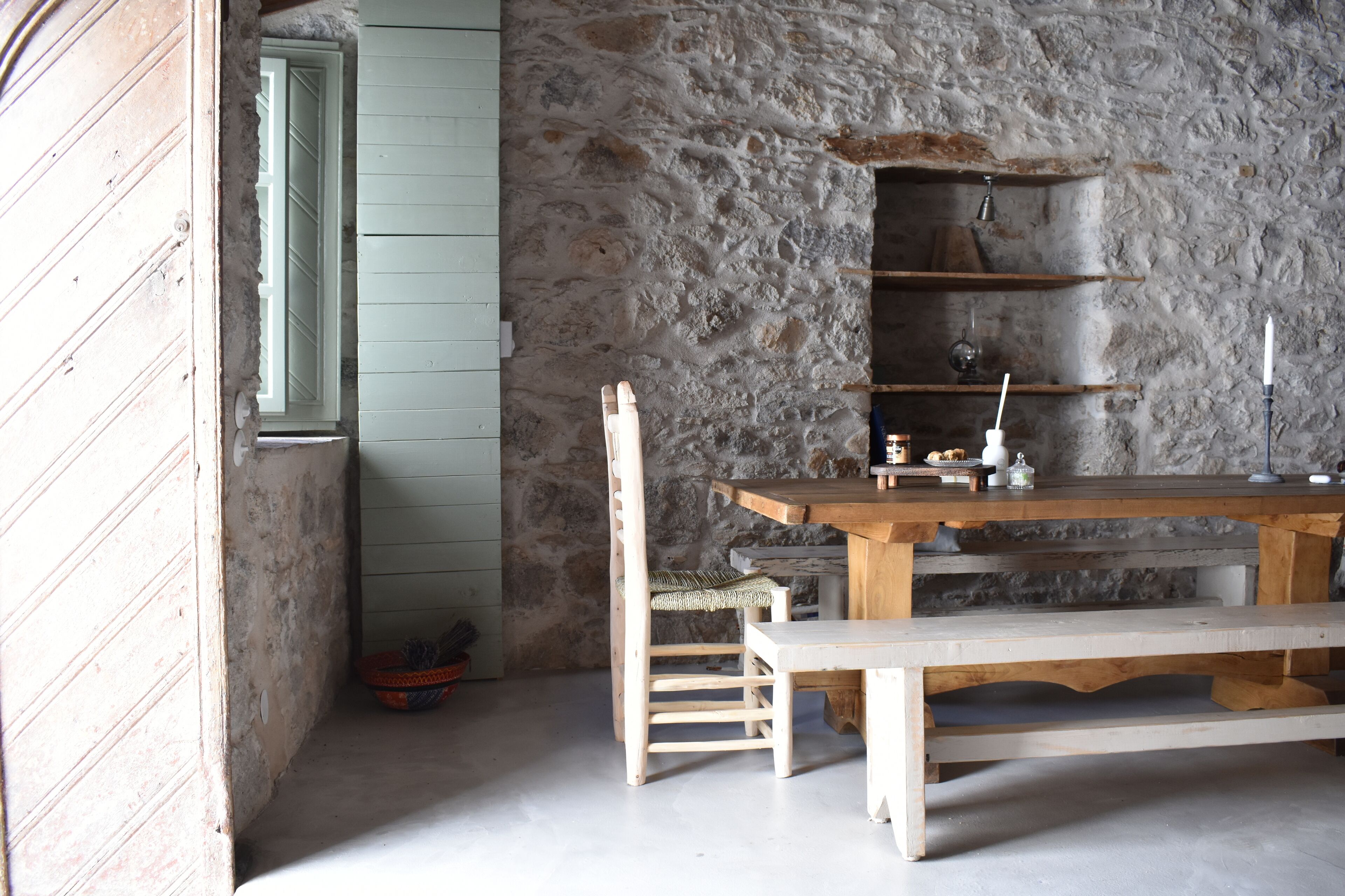 A rustic room with a wooden table, a bench, and a stone wall.