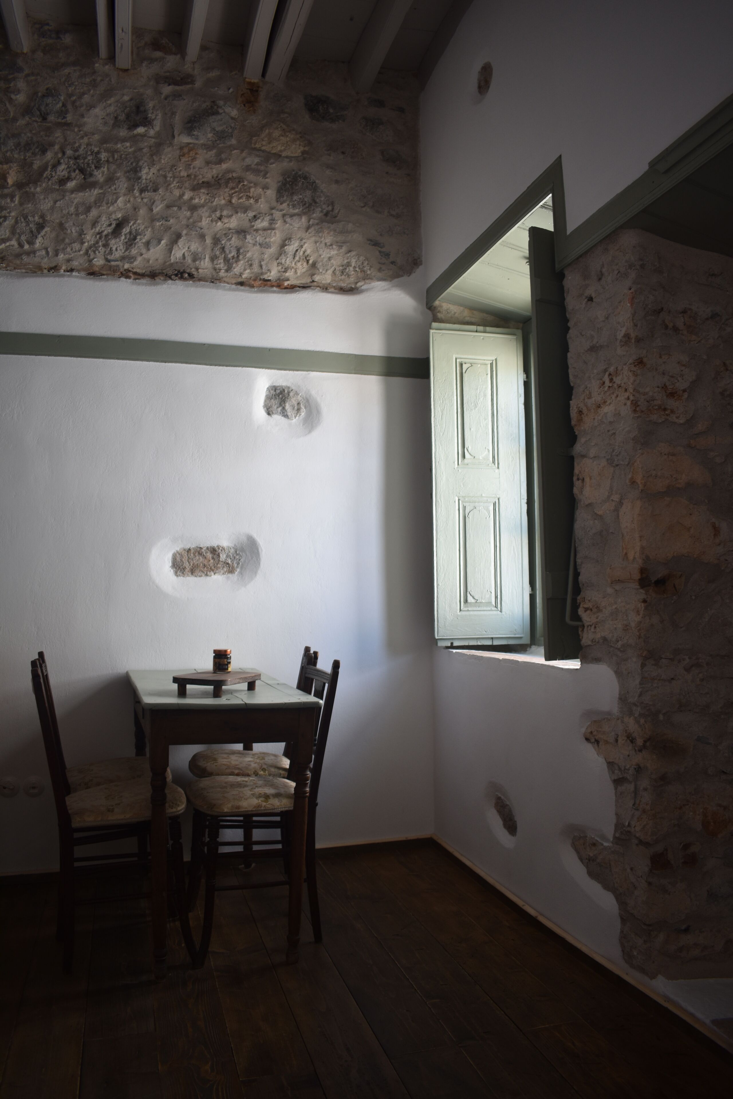 Une pièce avec un mur en pierre, une table en bois avec des chaises et une fenêtre dotée d’un cadre vert.