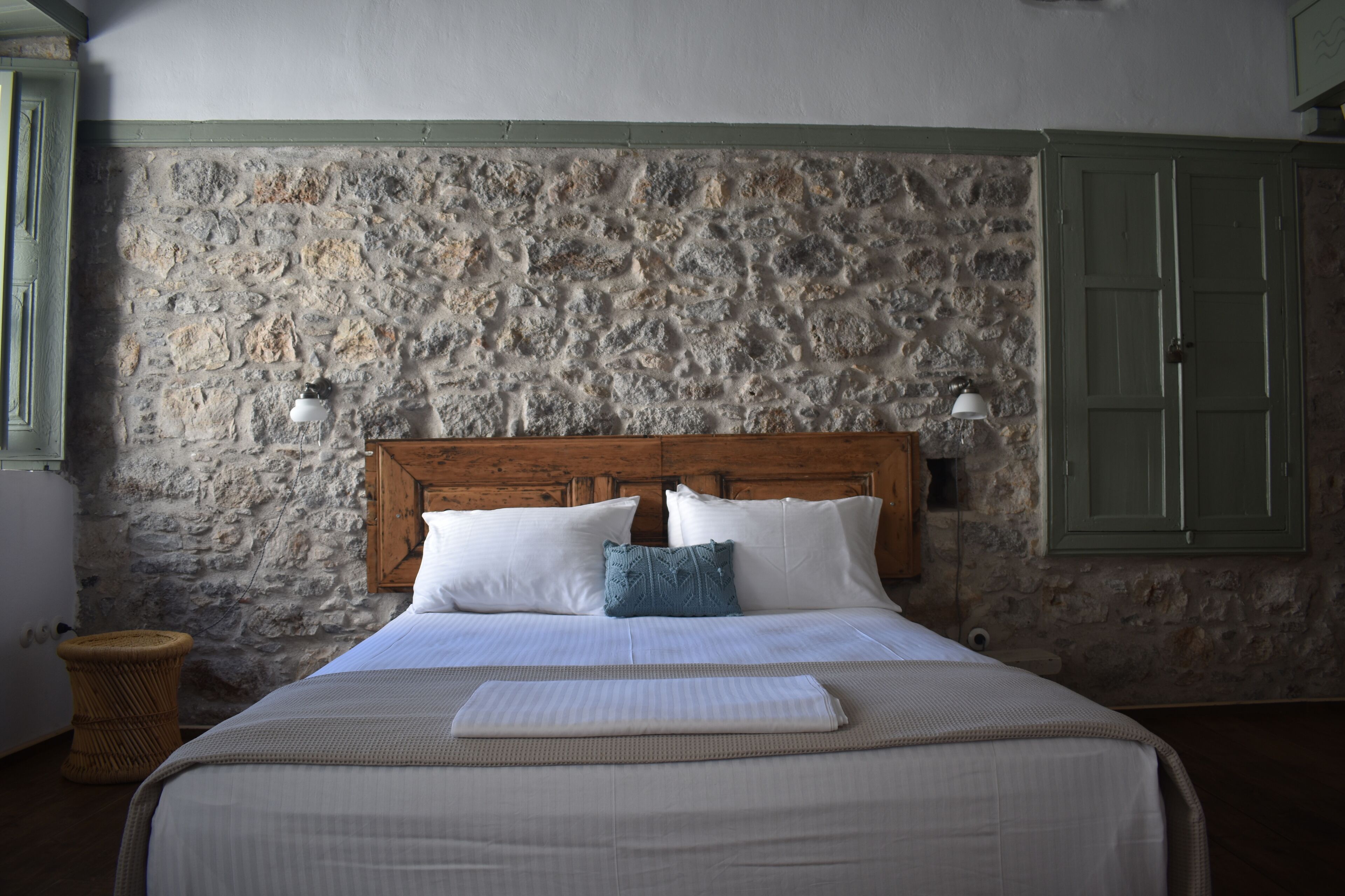 Ein Bett mit weißen Leinentüchern, einem hölzernen Kopfteil und einer Steinwand dahinter.