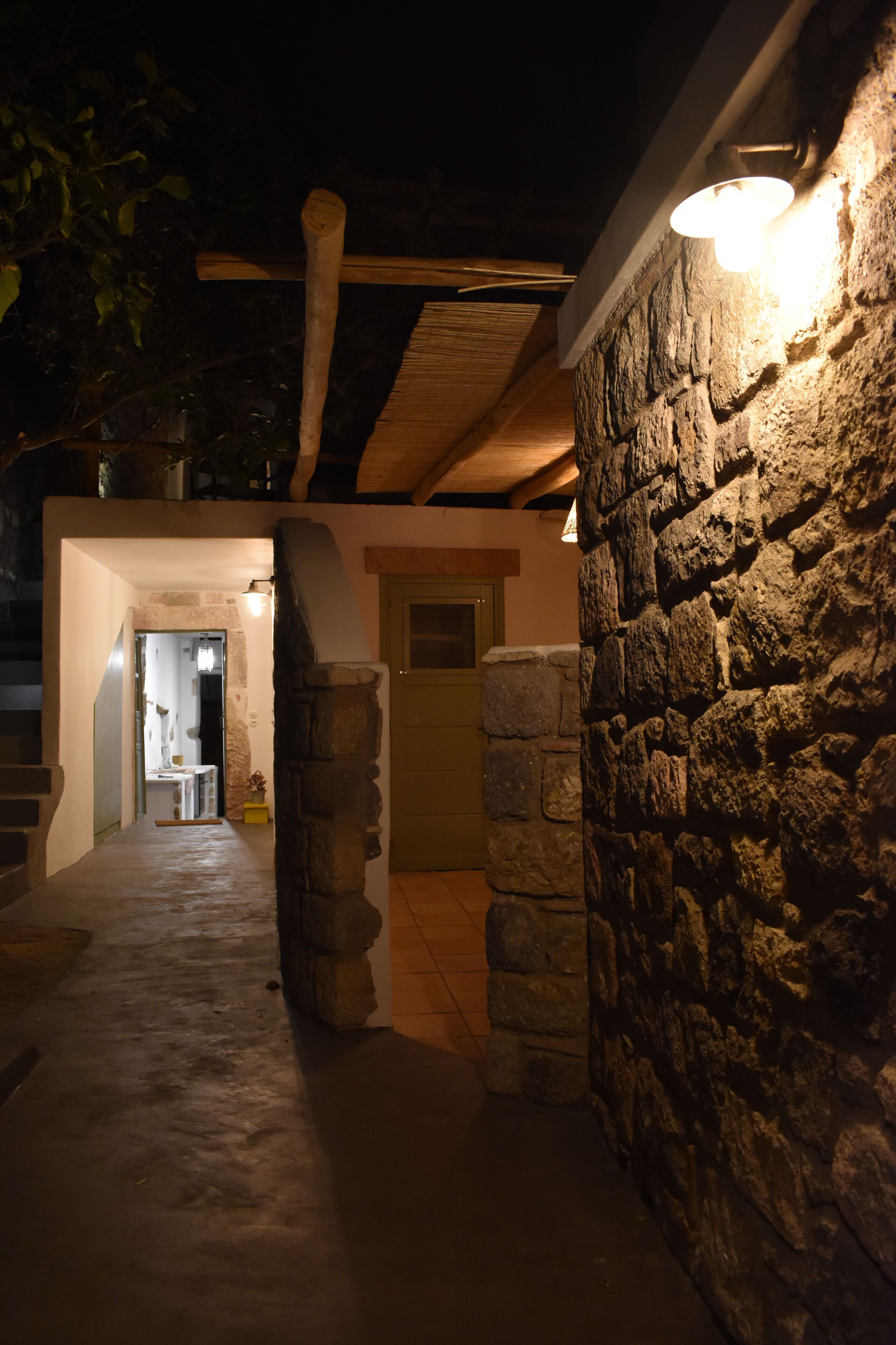 Un muro de piedra con una lámpara, una puerta de madera y un pasillo que conduce a una habitación.
