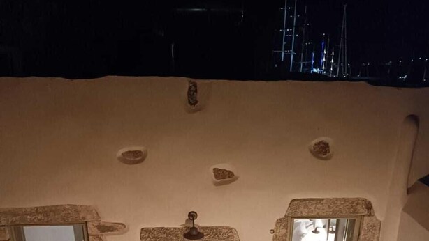 Una habitación acogedora con pared de piedra, puerta de madera, pequeña ventana con vistas, una mesa de comedor con sillas y una planta en maceta.
