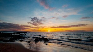 A beach scene with the sun setting over the ocean, rocks in the foreground, and a clear sky. - Maui Sunset Direct Ocean View with XL Lanai (Kihei)