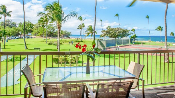 A balcony with a glass table and wicker chairs, overlooking a golf course and the ocean. - Maui Sunset Direct Ocean View with XL Lanai (Kihei)