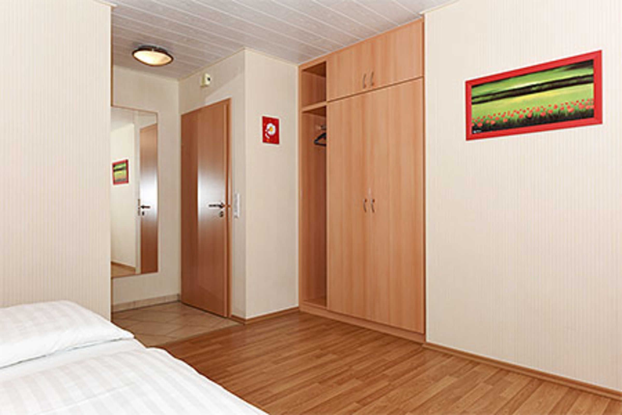 A bedroom with wooden flooring, a bed, a wardrobe, and a picture on the wall.