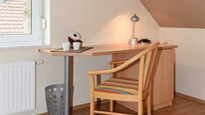 Une petite pièce agréable, avec un plafond en pente, un bureau en bois, une chaise, un radiateur et une fenêtre.
