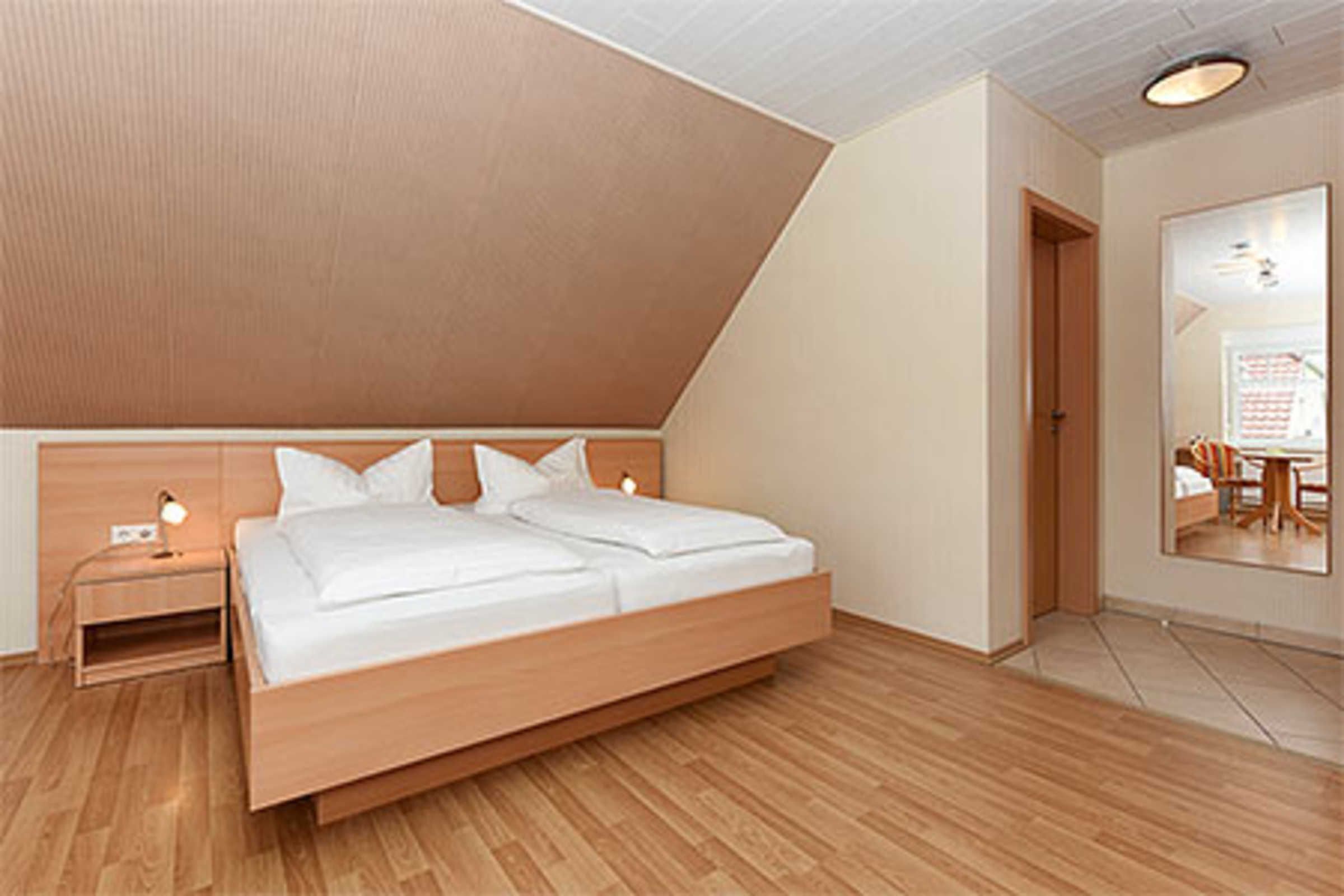 Une chambre moderne avec un lit en bois, une table de chevet et un miroir qui reflète un coin repas.