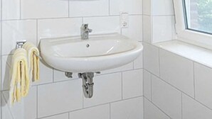 Une salle de bain avec un lavabo blanc, un miroir et une fenêtre.