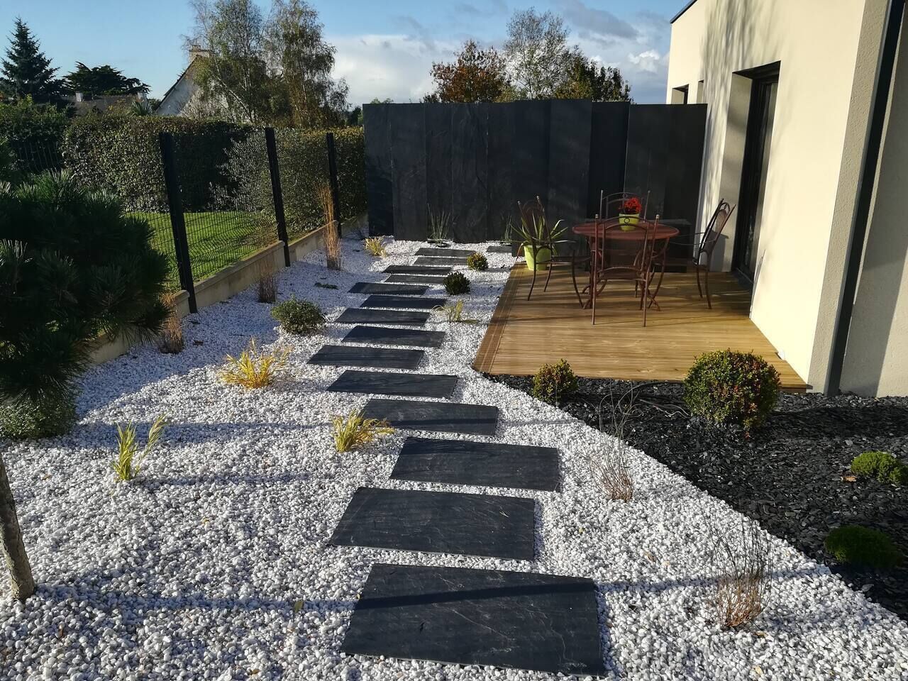 Ein Gartenweg führt zu einer Terrasse mit Tisch und Stühlen.