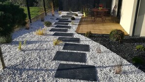 Un camí al jardí que condueix a una terrassa amb taula i cadires.
