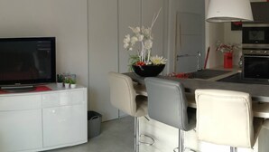Una cuina moderna amb zona de menjador, que destaca per una televisió de pantalla plana, un ram de flors i una gran làmpada penjant blanca.