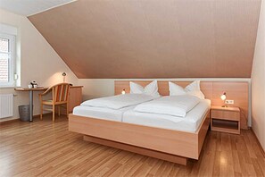 A bedroom with a sloped ceiling, a wooden bed, a bedside table with a lamp, a chair, and a desk.