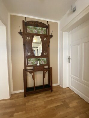 A wooden console table with a mirror and a vase, positioned against a beige wall in a room with wooden flooring and white doors.