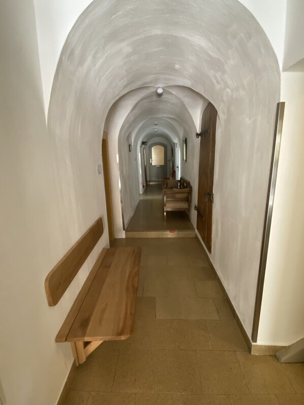 Een gang met een houten bank, een gewelfd plafond en een deur aan het einde.