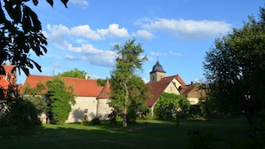 A courtyard with a church, stone buildings, and trees. - Holiday suite "Chalet" in the "Ferienhaus Burgcafé" (Betzenstein)