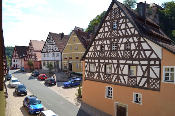 Une rue bordée de maisons traditionnelles à colombages, de voitures garées et d’un ciel dégagé.