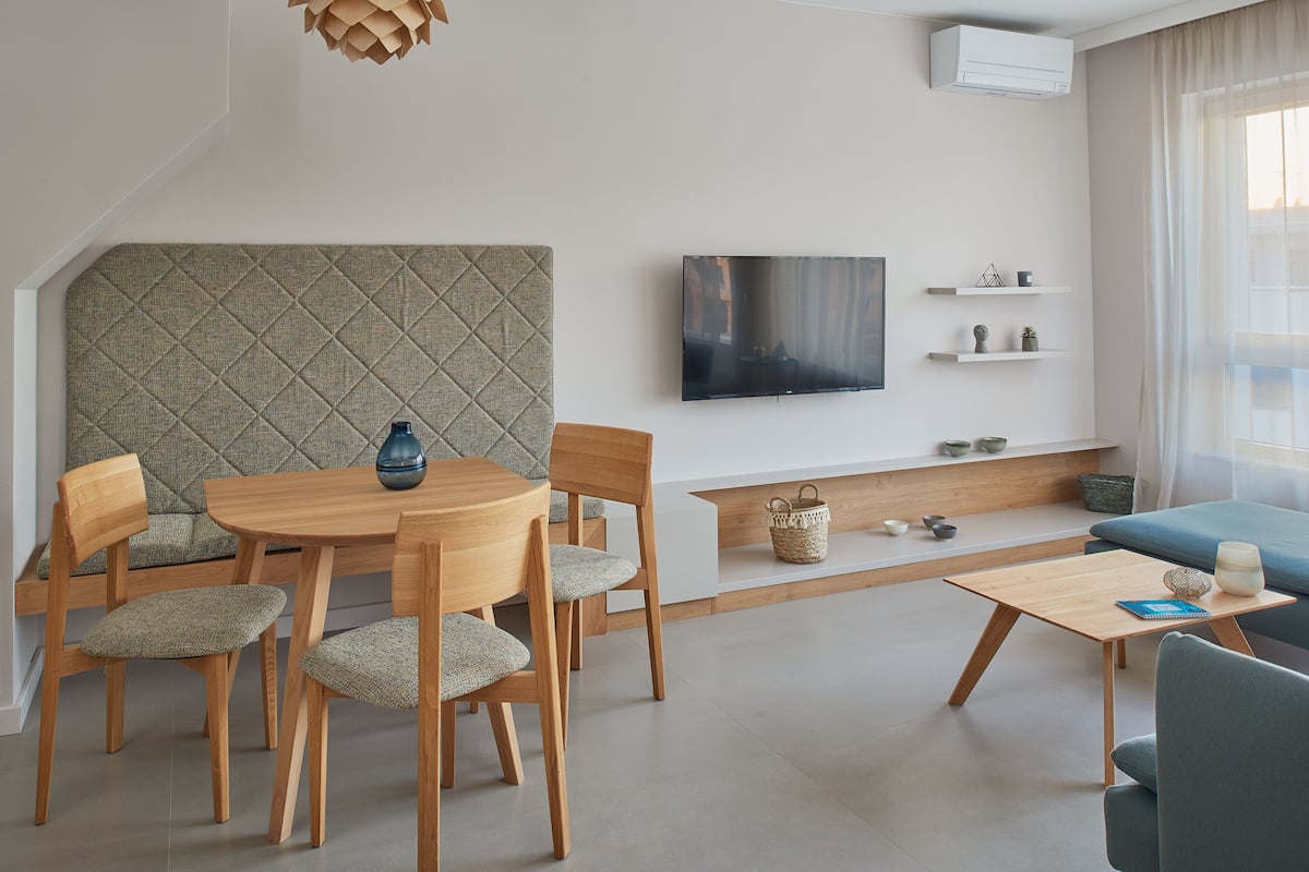 A modern living room with a dining area, a flat-screen TV mounted on the wall, and a cozy seating area with a sofa and chairs.