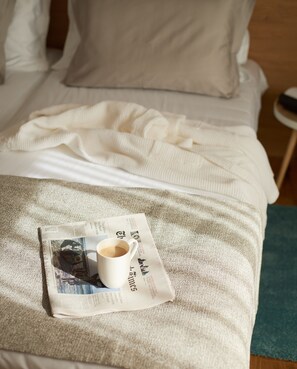 A bed with a white blanket and a newspaper with a coffee cup on it.