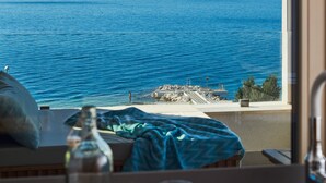 A room with a view of the sea, a window, a table with a bottle and glasses, and a bed with a pillow. - Eol Apartments Split (Split)